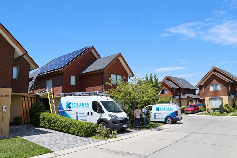 Vehículos de K Solares junto a viviendas con paneles solares en el techo.
